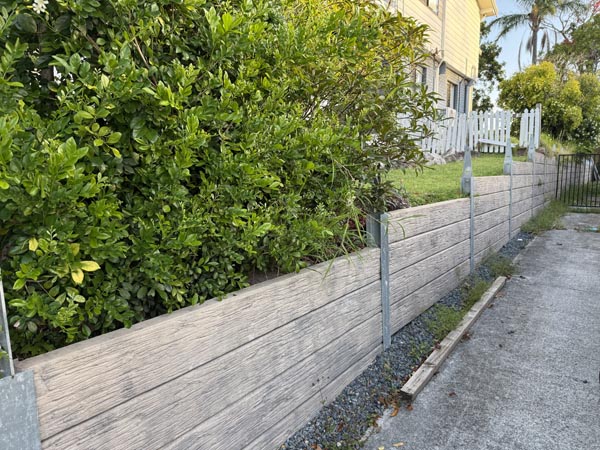 Concrete sleepers with a stamped timber effect pattern constructed as a structural retaining wall between glavanised H posts, finished with shark fin brackets